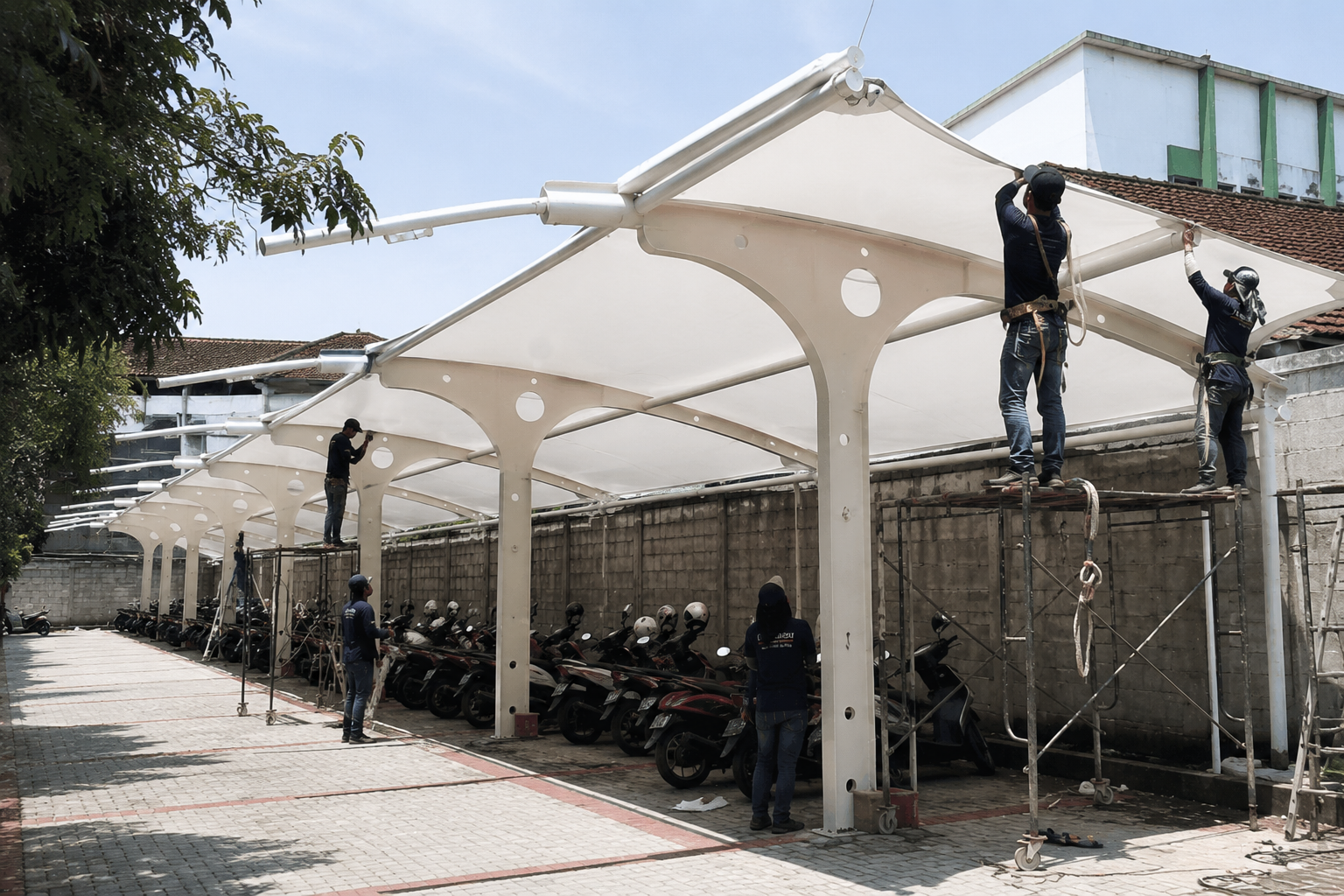 Pemasangan atap tenda membrane untuk parkir motor luas.